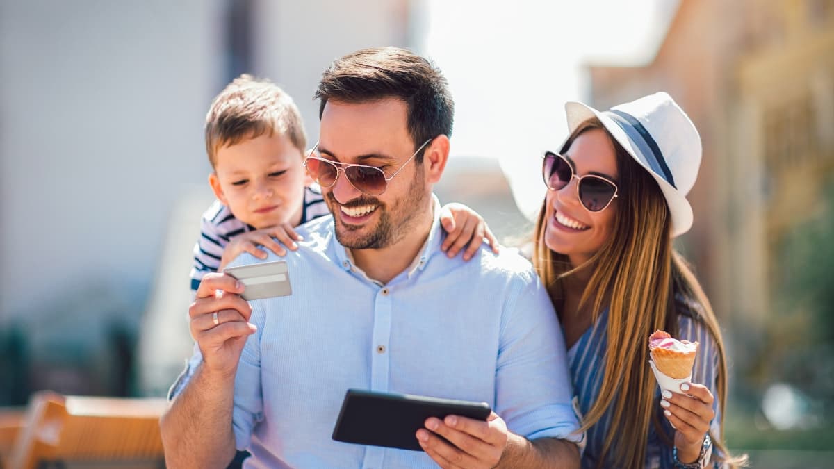 Family smiling outdoors while using a tablet and holding a credit card, exploring credit card rewards together.