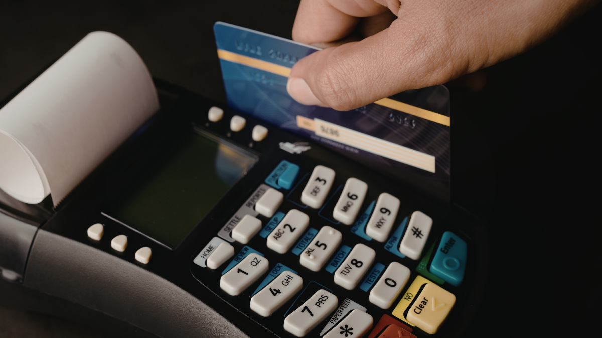 Close-up of a person inserting a credit card into a POS payment terminal with keypad and receipt printer, highlighting secure electronic payment transaction at checkout.
